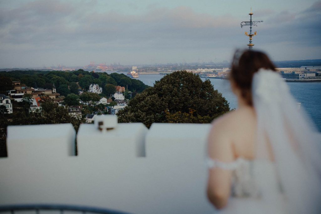 Eine Braut steht auf dem Turm vom Hotel Süllberg und genießt ihre Hochzeit in Hamburg.