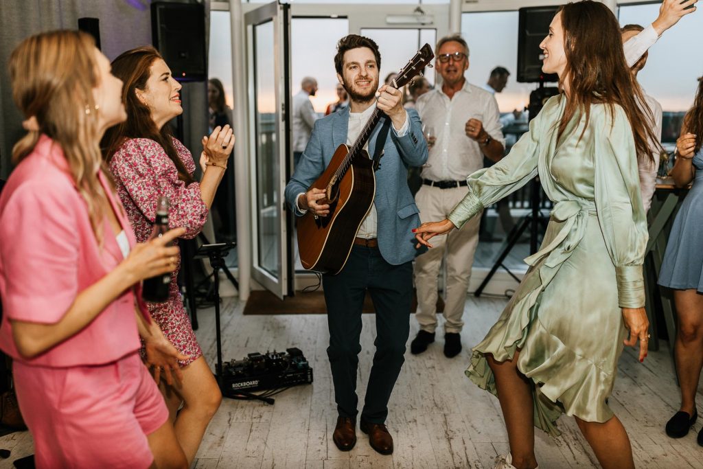Musiker mit Gitarre spielt zur Party einer Hochzeit. Gäste tanzen.