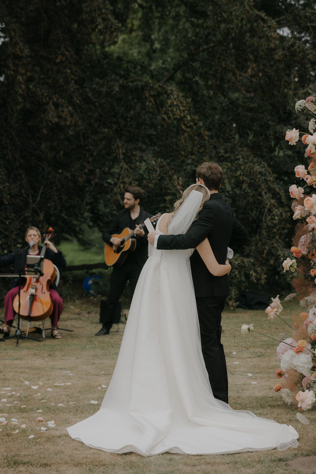 Musiker mit Cello und Gitarre spielen Live Musik zur Trauung auf Gut Bliestorf. Brautpaar umarmt sich und hört zu.