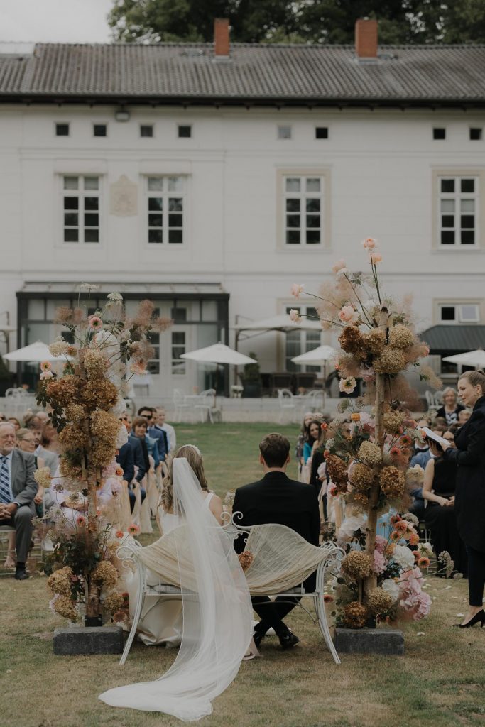 Hochzeitspaar sitzt bei der Trauung mit Blick auf die Gäste. Im Hintergrund das Gut Bliestorf.